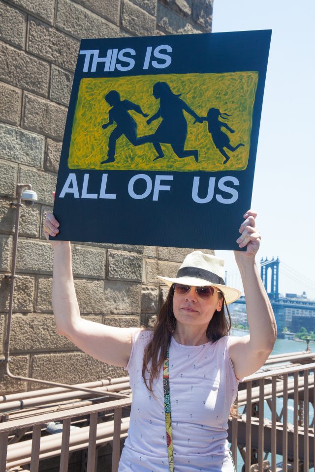 6/30/2018. New York City - March: “Families Belong Together.” A woman with a sign that reads: "This is all of us." People crossing the Brooklyn Bridge in support of refugee families. People’s protectors are marching from Foley Square in Manhattan to Cadman Plaza in Brooklyn. Credit: Photo by Javier Soriano/LoveIsAmor.com
