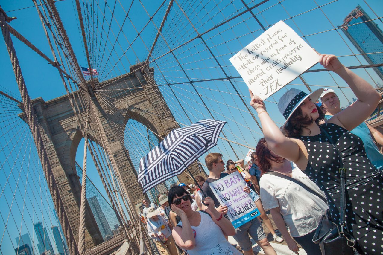 6/30/2018. New York City - March: “Families Belong Together.” Woman with a sign that reads: "The hottest places in hell are reserved for those who in time of moral crisis preserve their neutrality._J.F.K" People crossing the Brooklyn Bridge in support of refugee families. People’s protectors are marching from Foley Square in Manhattan to Cadman Plaza in Brooklyn. Credit: Photo by Javier Soriano/LoveIsAmor.com