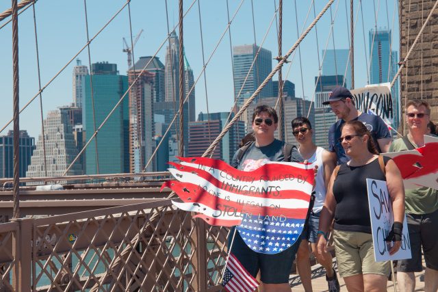 6/30/2018. New York City - March: “Families Belong Together.” A person with a sign that reads: "In a country founded by immigrants, no one is illegal on stolen land." People crossing the Brooklyn Bridge in support of refugee families. People’s protectors are marching from Foley Square in Manhattan to Cadman Plaza in Brooklyn. Credit: Photo by Javier Soriano/LoveIsAmor.com
