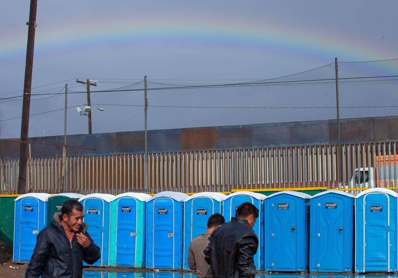 Tijuana, Baja California. Mexico. Thursday, November 29th, 2018. It was raining last night and it was raining all day today. Refugees in front of portable toilets and the rainbow in the sky. They are staying at Unidad Deportiva Benito Juárez (an improvised shelter for the caravans of immigrants). Refugees are fleeing violence in their countries in Central America. They want to apply for asylum in the United States of America. Credit: Photo by LoveIsAmor.com