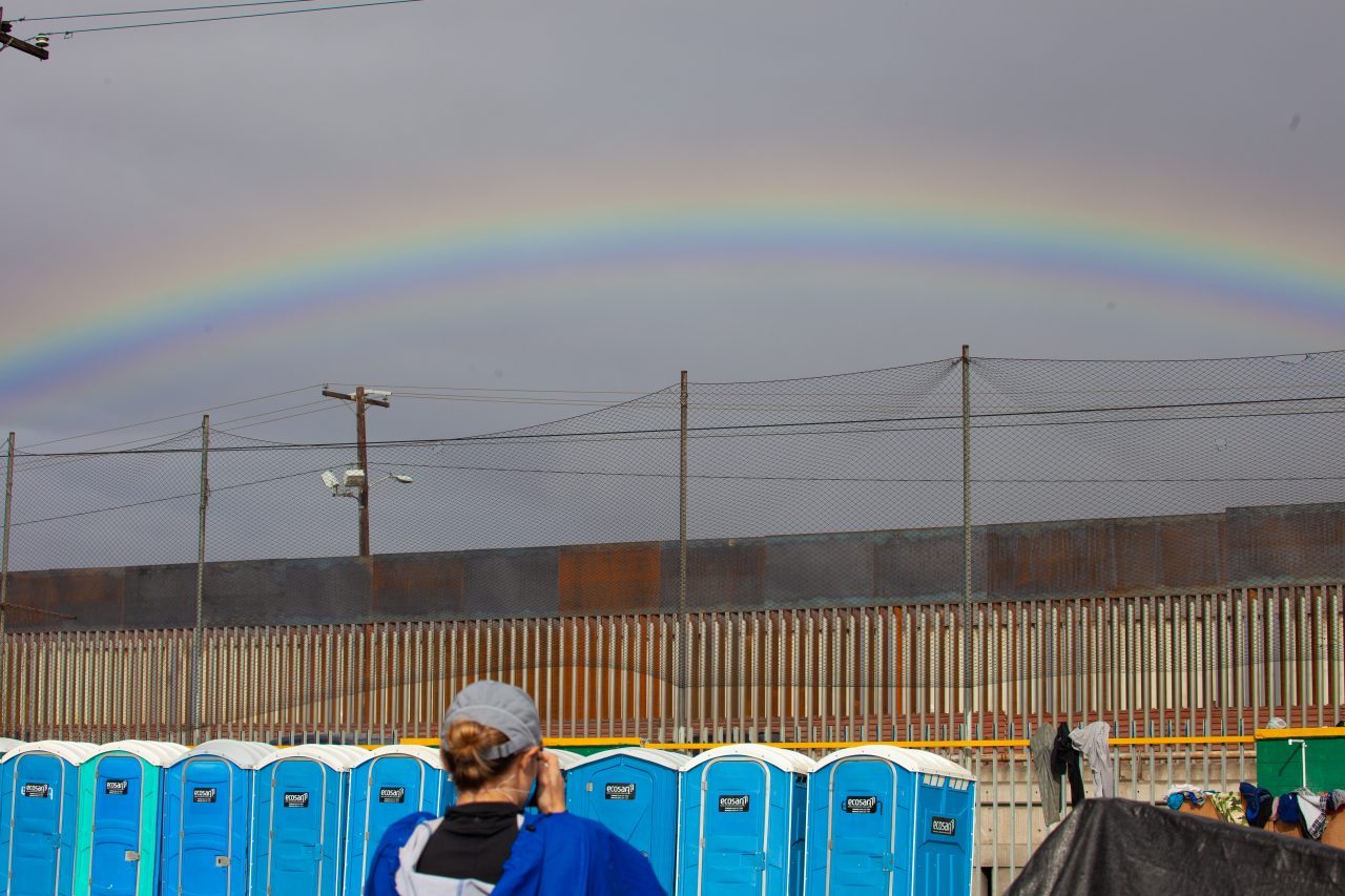 Tijuana, Baja California. Mexico. Thursday, November 29th, 2018. Female photographer taking a picture of the rainbow and the portable toilets. It was raining last night and it was raining all day today. Refugees are staying at Unidad Deportiva Benito Juárez (an improvised shelter for the caravans of immigrants). Refugees are fleeing violence in their countries in Central America. They want to apply for asylum in the United States of America. Credit: Photo by LoveIsAmor.com