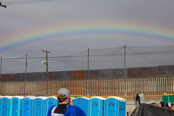Tijuana, Baja California. Mexico. Thursday, November 29th, 2018. Female photographer taking a picture of the rainbow and the portable toilets. It was raining last night and it was raining all day today. Refugees are staying at Unidad Deportiva Benito Juárez (an improvised shelter for the caravans of immigrants). Refugees are fleeing violence in their countries in Central America. They want to apply for asylum in the United States of America. Credit: Photo by LoveIsAmor.com